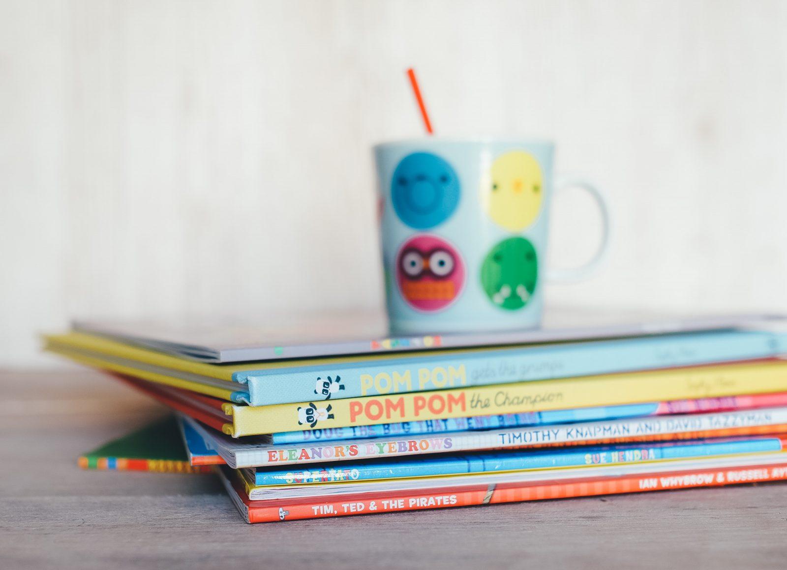 Photograph of children's books stacked, with a colourful cup on top