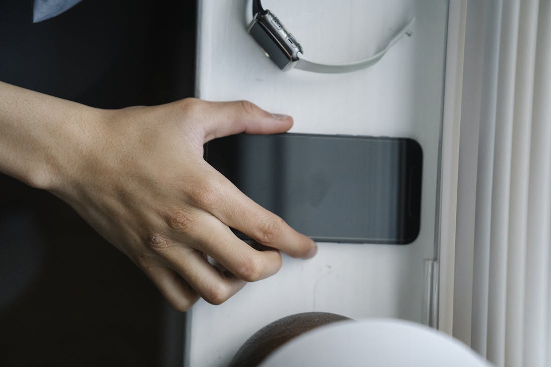 Top view of anonymous person taking cellphone with black screen from windowsill near wristwatch at home